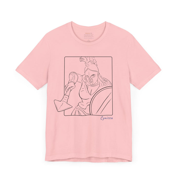 Pink t-shirt with a black line graphic of Cynisca in a dynamic close-up pose, wearing a helmet and holding spear and shield inside a rectangular frame, with the blue text 'Cynisca' below the design.