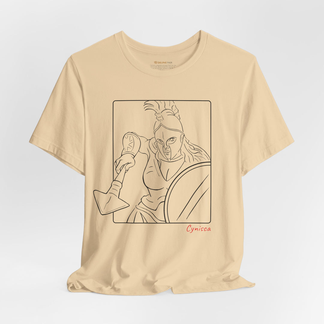 Soft-cream t-shirt with a black line graphic of Cynisca in a dynamic close-up pose, wearing a helmet and holding spear and shield inside a rectangular frame, with the red text 'Cynisca' below the design.